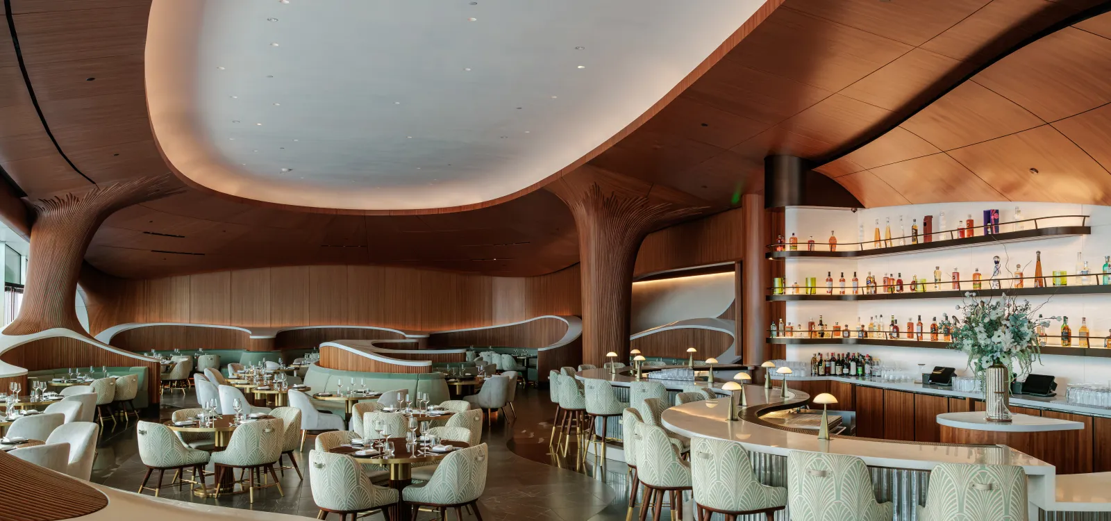 Skywalker Grill restaurant interior with curved wooden ceilings, contemporary seating and a central bar with illuminated bottle displays.