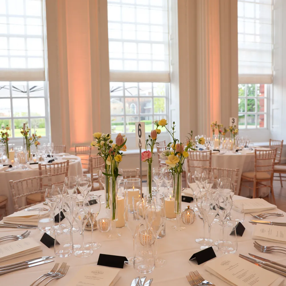 Round tables set with white linens, glassware, candles, and floral centrepieces in the Orangery Room at Kensington Palace