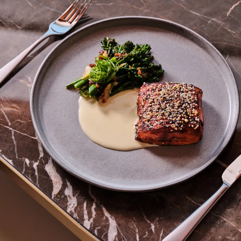 Sesame-crusted glazed salmon served with tenderstem broccoli and a creamy sauce at Skywalker Grill.