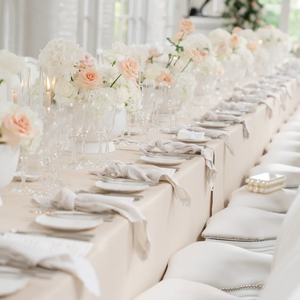 An elegant dining table at The Orangery, Holland Park, dressed with white and blush floral arrangements, fine glassware, candles and neutral linen, with white upholstered chairs.