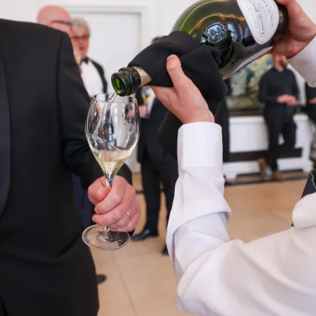 Server pouring Champagne from a bottle into a flute glass held by a guest