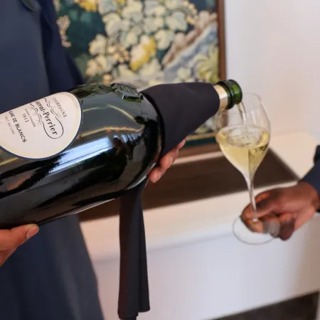 Close-up of a server pouring Champagne from a large bottle into a flute glass, with another person holding the glass in a refined indoor setting