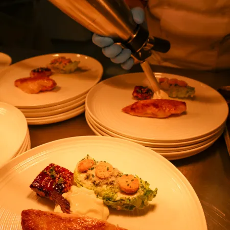 Chef using a cream whipper to finish plating the main dish