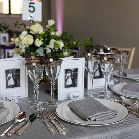 Elegant banquet table set for an anniversary lunch at Queen's House, featuring silver-rimmed glassware, floral centrepieces, personalised place settings, and refined tableware in the Great Hall.
