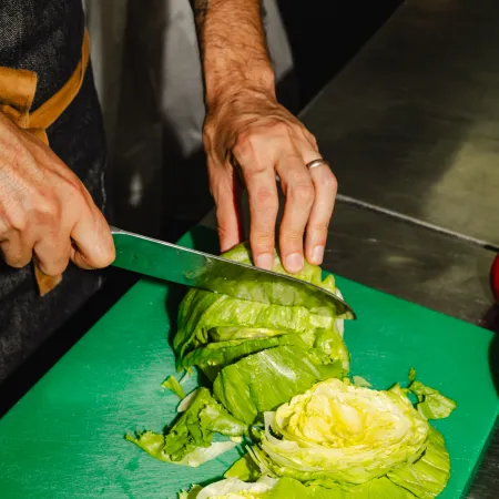 Chef chopping fresh iceberg lettuce on a green chopping board in a commercial kitchen.