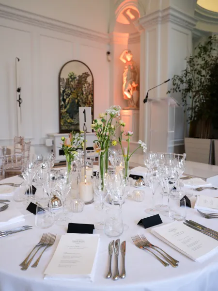 ound table set with glassware, candles, and floral centrepieces in the Orangery Room at Kensington Palace, with a lectern and classical statue in the background.