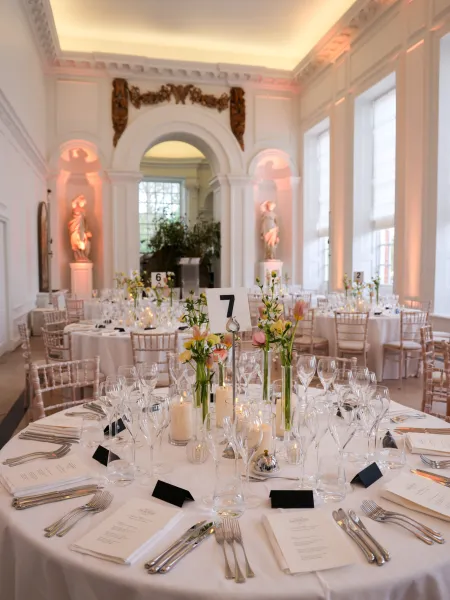 Round tables set with white linens, glassware, candles, and floral centrepieces in the Orangery Room at Kensington Palace