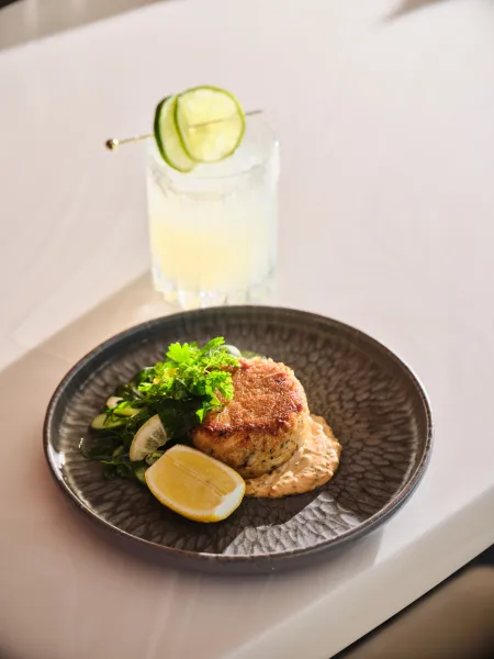 Seared seafood dish served with greens, lemon and a creamy sauce, alongside a lime-garnished cocktail at Skywalker Grill.