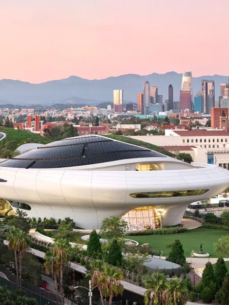 Aerial view of the Lucas Museum of Narrative Art in Los Angeles at dusk, with the city skyline in the background.