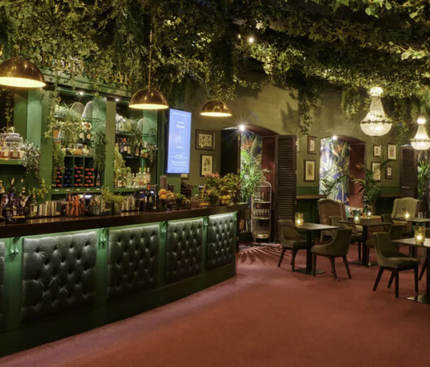 Interior of the Royal Albert Hall’s Kensington Garden bar, featuring greenery, chandeliers and lounge seating