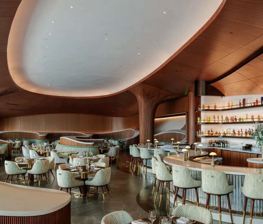 Skywalker Grill restaurant interior with curved wooden ceilings, contemporary seating and a central bar with illuminated bottle displays.