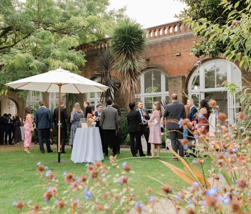 Guests on the lawn at The Orangery, Holland Park, surrounded by lush greenery, mature trees and the venue’s historic brick arches.