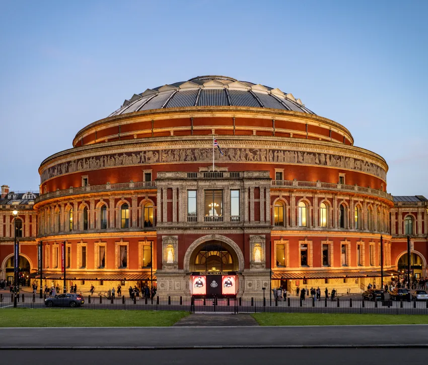 Royal Albert Hall illuminated at dusk, showcasing its grand circular façade and ornate architectural details against a clear evening sky. Credit: Annabel Moeller
