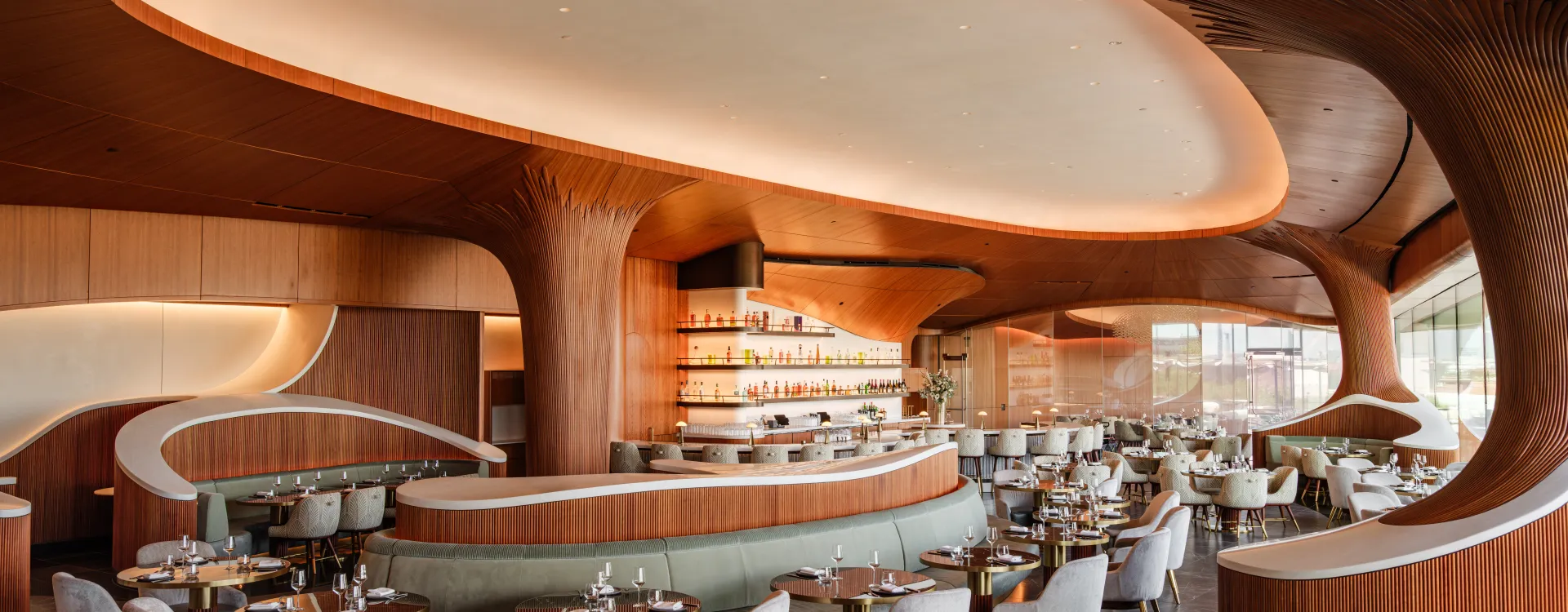 Skywalker Grill restaurant interior with curved wooden ceilings, contemporary seating and a central bar with illuminated bottle displays.
