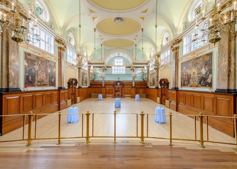The Main Hall at Chelsea Old Town Hall, featuring ornate gold detailing, high arched ceilings, large windows, wood panelling, historic murals and elegant chandeliers.
