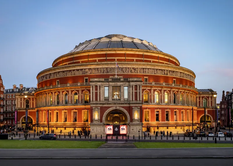 Royal Albert Hall illuminated at dusk, showcasing its grand circular façade and ornate architectural details against a clear evening sky. Credit: Annabel Moeller